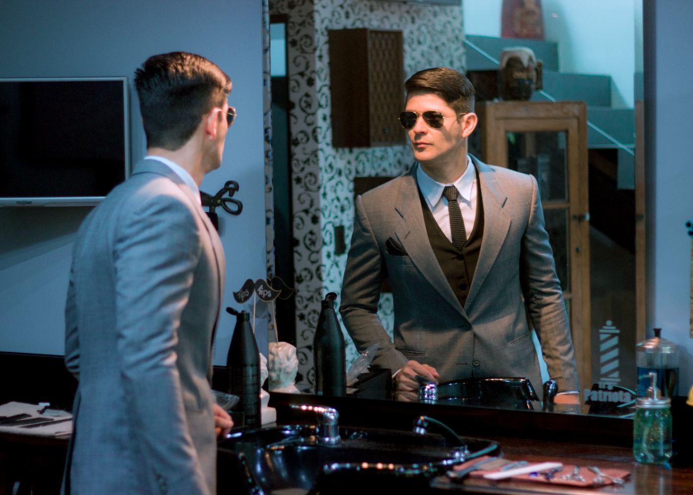 Caballero con traje beige claro y chaleco café revisando su reflejo en espejo de barbería