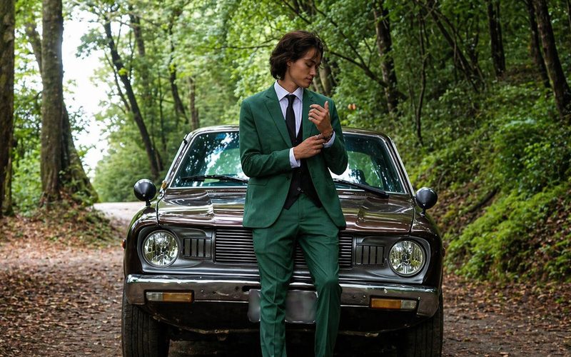 Caballero con traje verde de tres piezas frente a un vehículo clásico